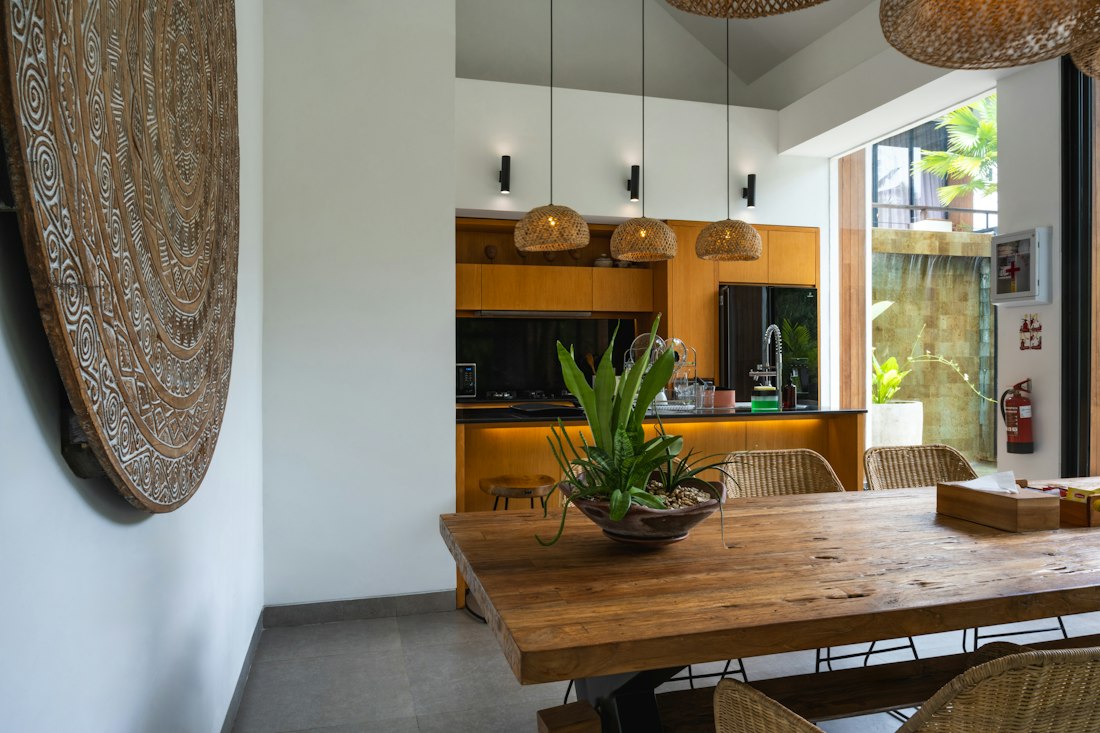 Cuisine ouverte avec une longue table en bois, chaises en osier et suspensions tressées.